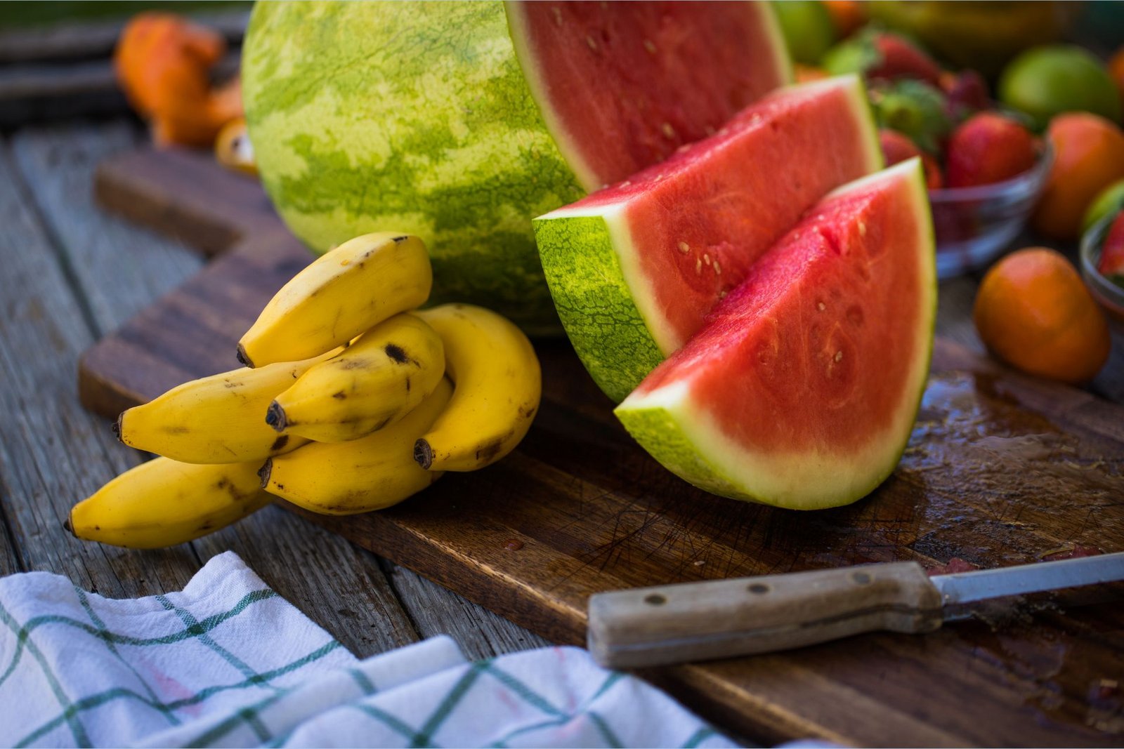 Banány bohaté na draslík leží na prkénku vedle plátků melounu bohatých na L-citrulin.